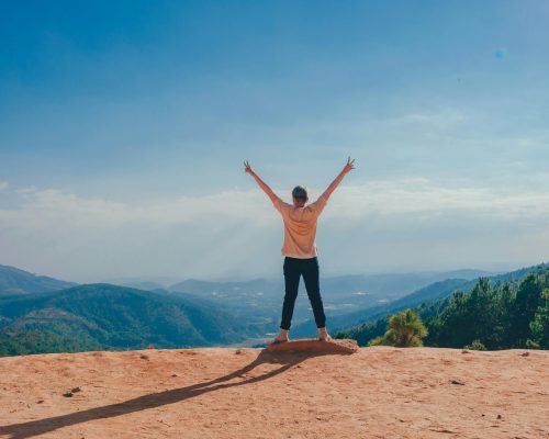A woman stands victoriously on a mountain top with arms raised, embracing nature and freedom.