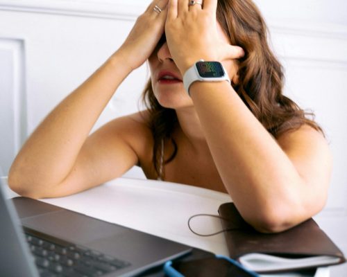 Woman showing stress or tiredness with hands on face at a desk with a laptop.