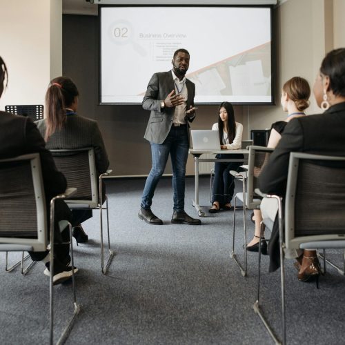 Diverse group attending a business seminar with a presenter and screen display.