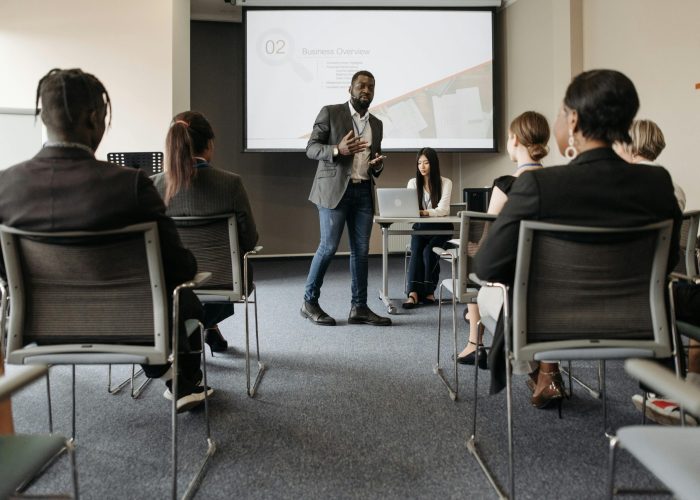 Diverse group attending a business seminar with a presenter and screen display.